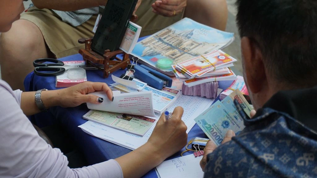 Detalle del puesto de lotería con billetes de colores apilados y monedas sobre la madera gastada.